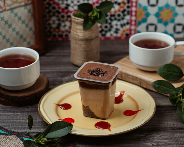 Mousse di crema al cioccolato in una tazza con due tazze di tè nero