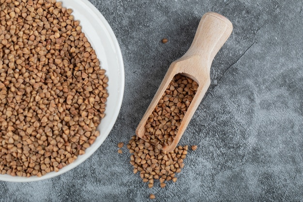 Mucchio di grano saraceno crudo sul piatto bianco con il cucchiaio