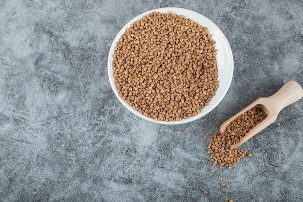 Mucchio di grano saraceno crudo sul piatto bianco con il cucchiaio