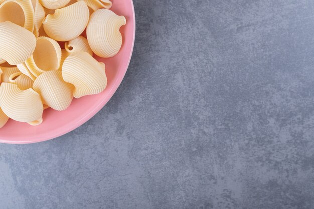 Mucchio di pasta conchiglie sul piatto rosa.