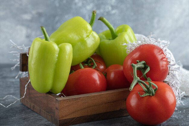 Mucchio di verdure fresche sul cesto di legno su sfondo grigio.