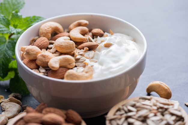 Muesli fatti in casa o muesli, ciotola di muesli d'avena con yogurt, mandorle, anacardi, menta e noci sulla tavola da roccia nera per una sana colazione, spazio copia. Concetto di menu per la colazione sana.