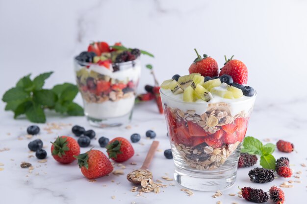 Muesli fatto in casa, ciotola di muesli d'avena con yogurt, mirtilli freschi, gelso, fragole, kiwi, menta e noci per una sana colazione, copia spazio. Concetto di colazione sana. Mangiare pulito.