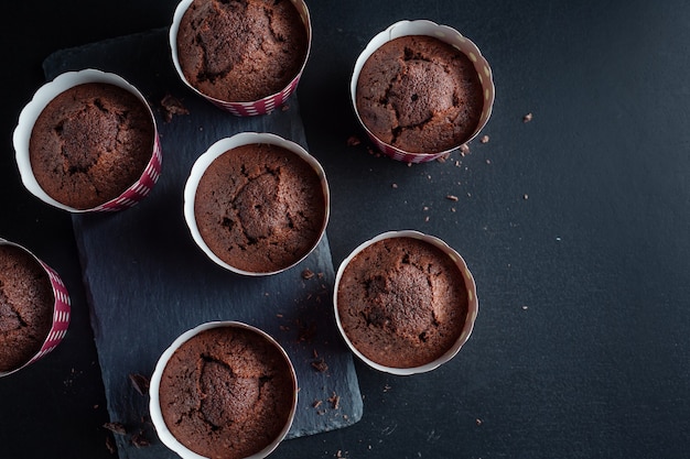 Muffin al cioccolato appetitosi gustosi in tazze su sfondo scuro.