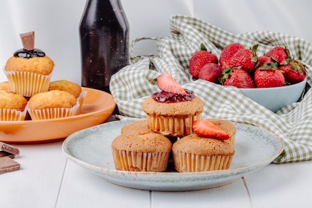 Muffin di vista frontale con le fragole e muffin con cioccolato sui piatti con le fragole