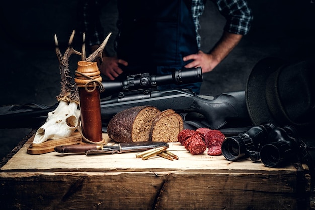 Munizioni da caccia retrò di fucile e binocolo. Deliziosa salsiccia e pane nero su un tavolo di legno.