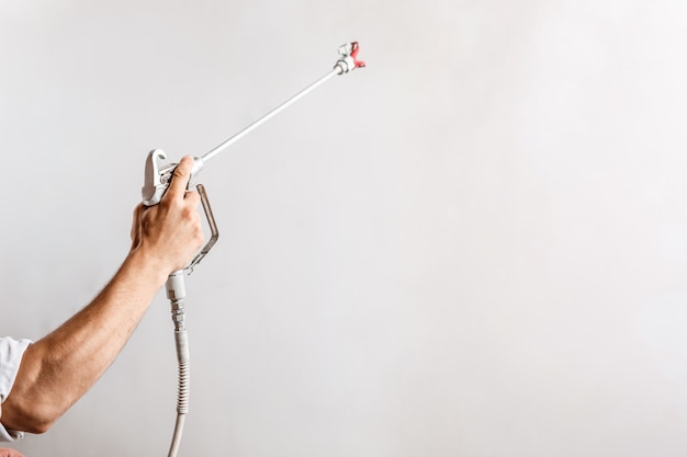 Muro dipinto operaio con pistola a spruzzo di colore bianco.