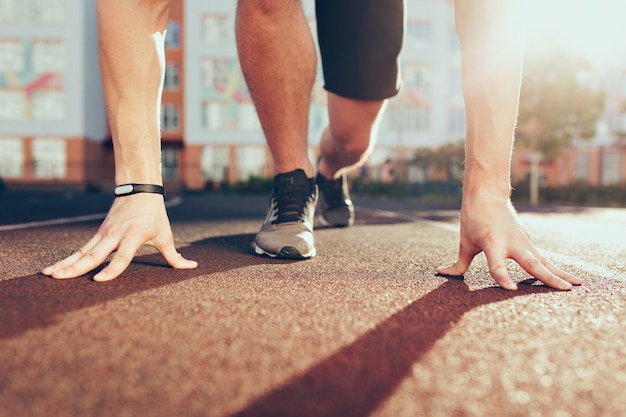 Muscoli, mani, luce solare, gambe in scarpe da ginnastica di un ragazzo forte allo stadio al mattino. Ha la preparazione in partenza.