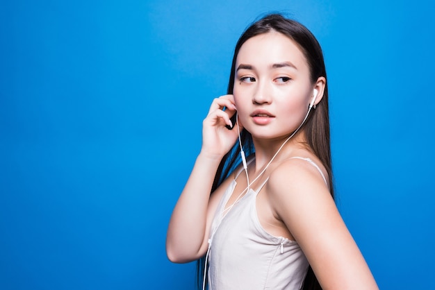Musica d'ascolto della giovane donna asiatica attraente sulla parete blu