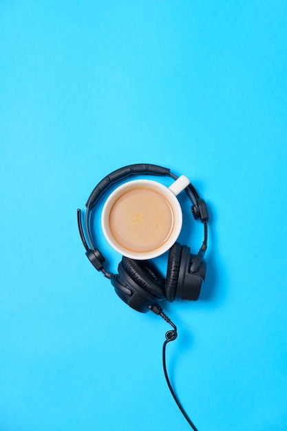 Musica o podcast di sottofondo con cuffie e tazza di caffè su un tavolo blu piatto Vista dall'alto piatto