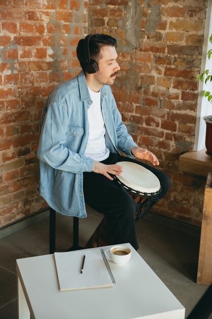 Musicista caucasico che suona il tamburo a mano durante il concerto online a casa isolato e messo in quarantena.