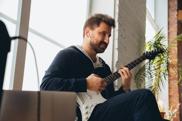 Musicista caucasico suonare la chitarra durante il concerto online a casa isolato e messo in quarantena, improvvisazione allegra