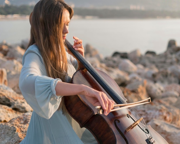 Musicista che suona il violoncello al tramonto sulle rocce