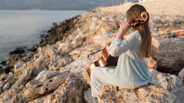 Musicista che suona il violoncello al tramonto sulle rocce