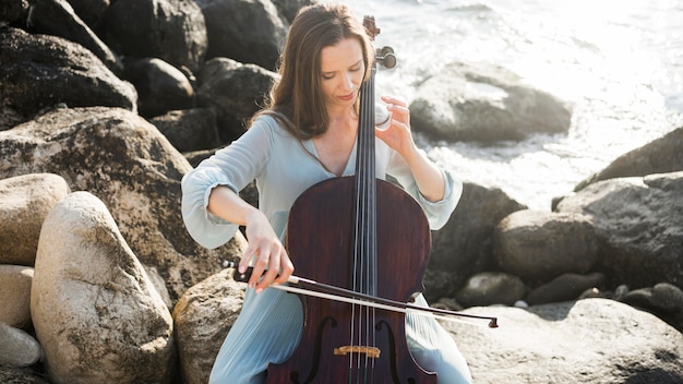 Musicista che suona il violoncello in riva all'oceano