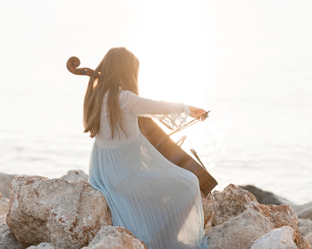 Musicista che suona il violoncello sulle rocce in riva al mare