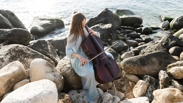 Musicista femminile sulle rocce che gioca violoncello dall'oceano