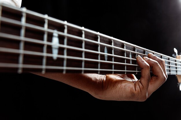 Musicista jazz afroamericano bello suonare il basso in studio su sfondo nero. Concetto di musica. Giovane ragazzo attraente gioioso che improvvisa. Close-up retrò ritratto.