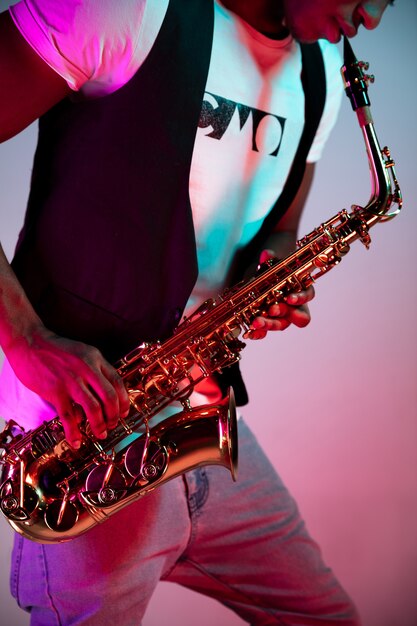 Musicista jazz afroamericano bello suonare il sassofono in studio su uno sfondo al neon. Concetto di musica. Giovane ragazzo attraente gioioso che improvvisa. Close-up retrò ritratto.