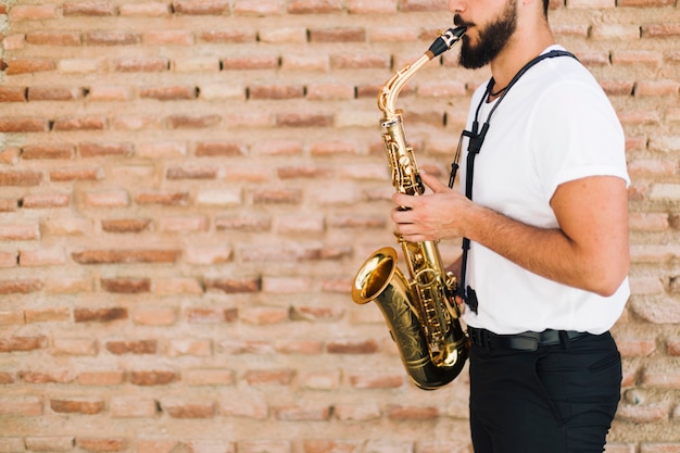 Musicista lateralmente che gioca il sax con il fondo del muro di mattoni