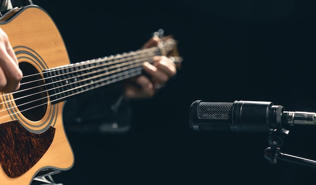 Musicista maschio che suona la chitarra acustica dietro il microfono in uno studio di registrazione