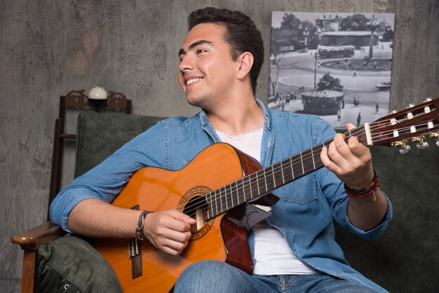 Musicista sorridente che suona la chitarra e che si siede sul divano. Foto di alta qualità