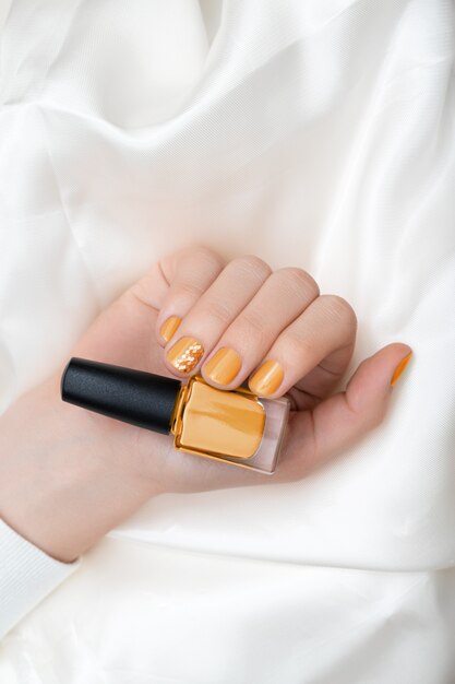 Nail design giallo. Mano femminile con manicure glitterata.