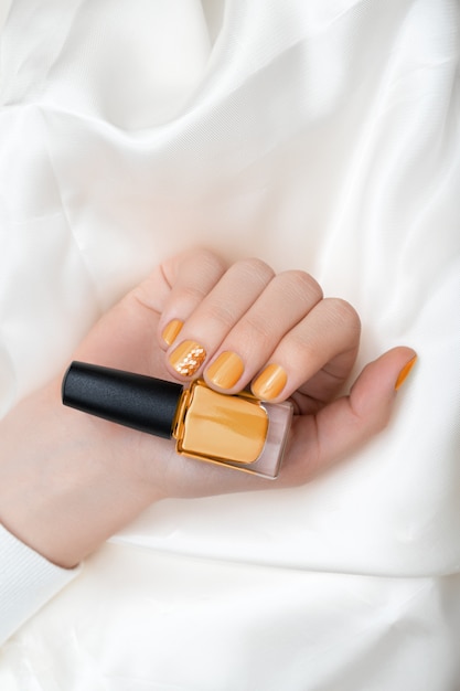 Nail design giallo. Mano femminile con manicure glitterata.