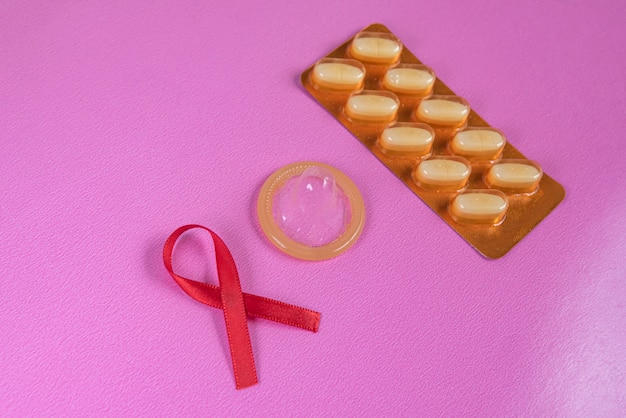 Nastro rosso, preservativo, siringa e medicina sul tavolo rosa