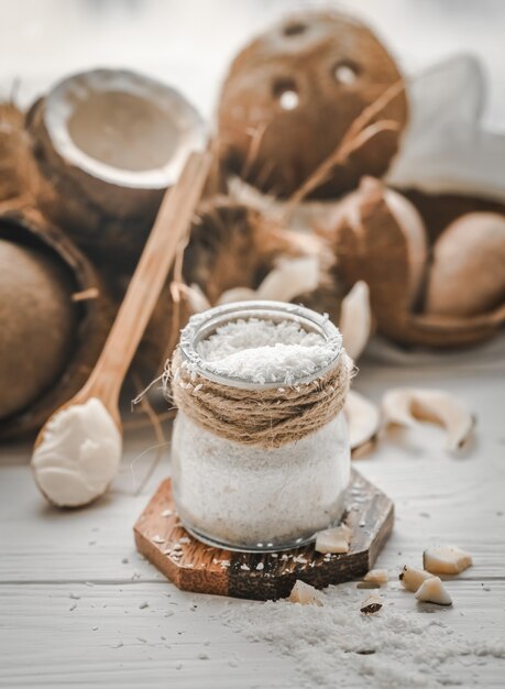 Natura morta con cocco e fiocchi di cocco in cucchiai di legno e vaso di vetro su fondo in legno