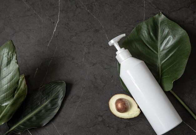 Natura morta con mockup di bottiglia dispenser cosmetico bianco con avocado e foglie vista dall'alto. Concetto di bellezza e igiene.