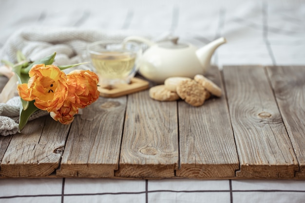 Natura morta con una tazza di tè, una teiera, biscotti e un mazzo di tulipani