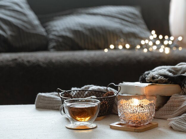 Natura morta con una tazza di tè, una teiera, libri e una candela accesa in un candeliere con bokeh.