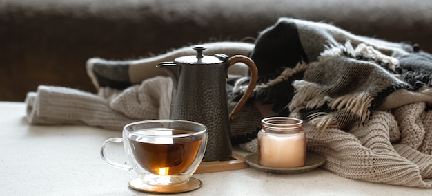 Natura morta con una tazza di tè, una teiera, una candela in un candeliere e cose lavorate a maglia da vicino.
