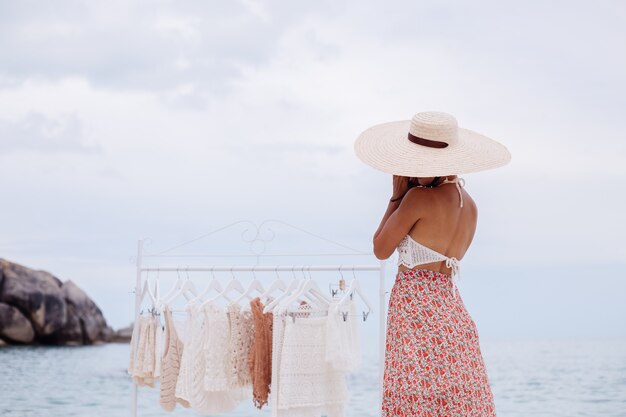 Negozio all'aperto sulla spiaggia per la scelta di vestiti lavorati a maglia donna cosa comprare da appendiabiti Concetto di abbigliamento lavorato a maglia estivo