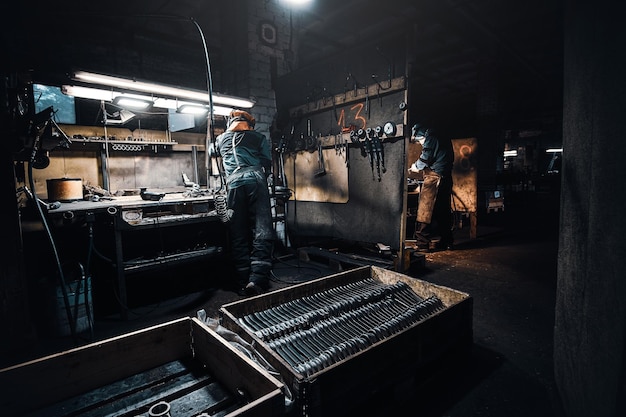 Nell'officina buia, un lavoratore esperto in uniforme protettiva sta lavorando con il metallo.