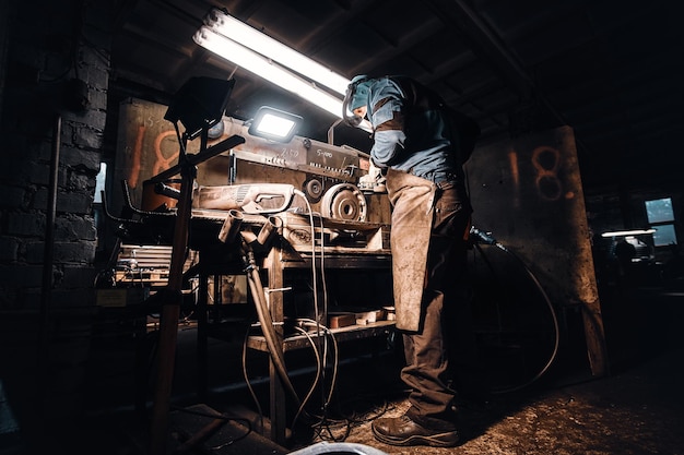 Nella fabbrica di metallo scuro un uomo impegnato sta lavorando sul suo posto di lavoro.