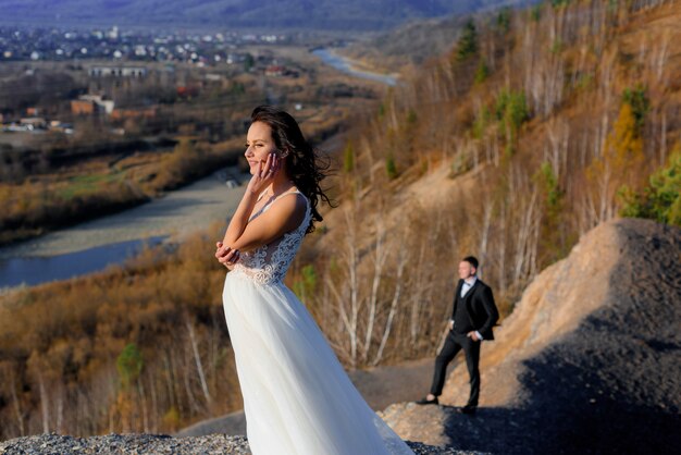 Nella soleggiata giornata autunnale sulla collina è in piedi la sposa in primo piano e uno sposo sfocato sullo sfondo