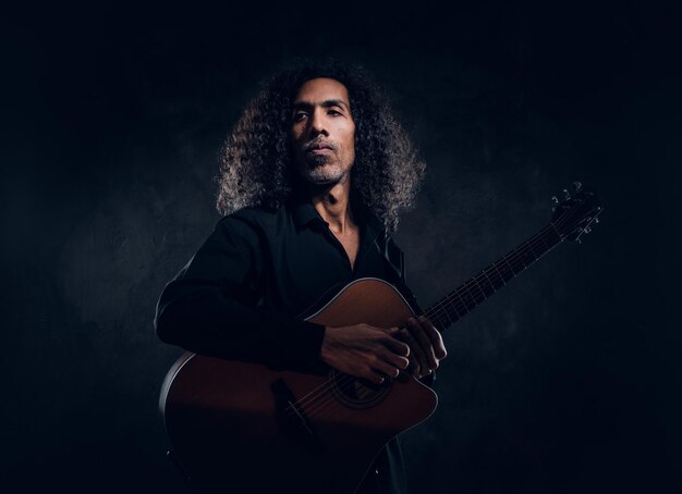 Nello studio fotografico scuro l'uomo di mezza età riccio sta posando con la chitarra per il fotografo.