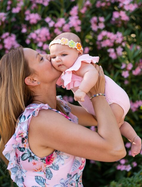 Neonata con vestiti a maglia rosa e un accessorio per la testa tra le braccia di una donna