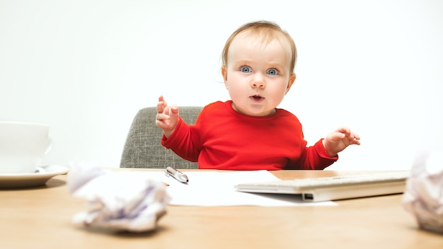 Neonata felice del bambino che si siede con la tastiera del calcolatore o del laptop moderno isolata su uno studio bianco