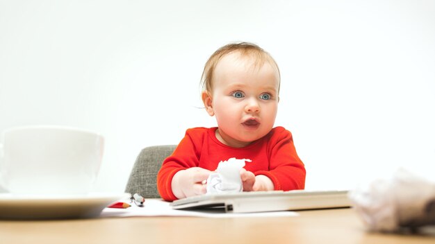 Neonata felice del bambino che si siede con la tastiera del calcolatore o del laptop moderno isolata su uno studio bianco