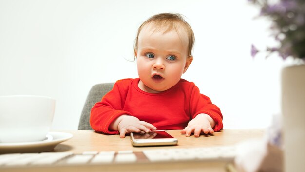Neonata felice del bambino che si siede con la tastiera del calcolatore o del laptop moderno nel bianco
