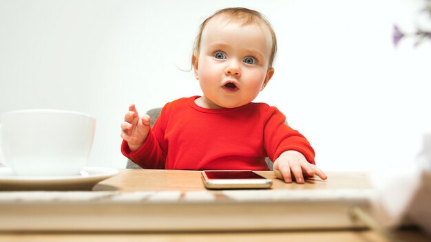 Neonata felice del bambino che si siede con la tastiera del computer o del computer portatile moderno in studio bianco