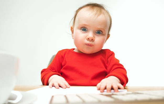 Neonata felice del bambino che si siede con la tastiera del computer o del laptop moderno in studio bianco