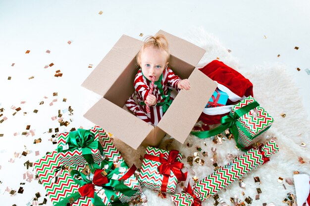 Neonata sveglia 1 anno di età che si siede nella casella sopra la priorità bassa della decorazione di Natale. Vacanza, celebrazione, concetto di bambino