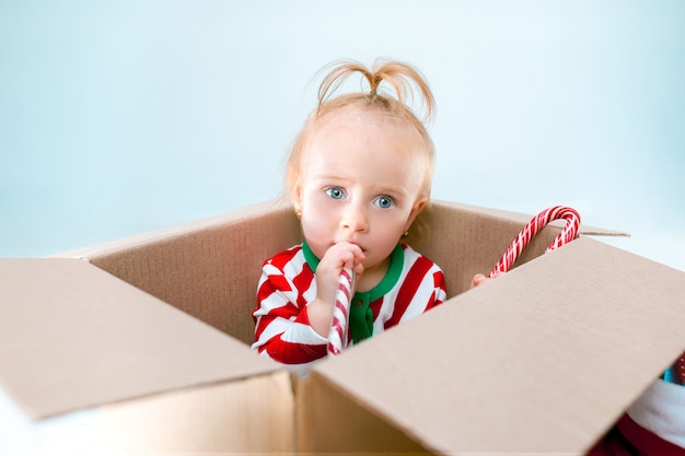 Neonata sveglia 1 anno di età seduto nella casella su sfondo natalizio. Vacanza, celebrazione, concetto di bambino