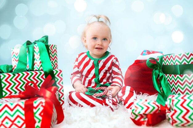 Neonata sveglia 1 anno di età vicino al cappello della santa che propone sopra il Natale con la decorazione. Seduto sul pavimento con la palla di Natale