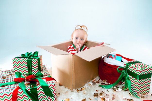 Neonata sveglia che si siede nella casella sopra il fondo di Natale. Vacanza, celebrazione, concetto di bambino