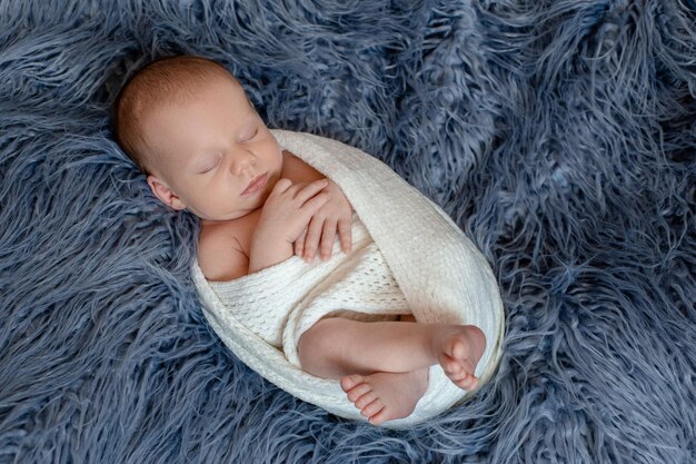 Neonato a letto. Bambino appena nato che dorme sotto una coperta lavorata a maglia bianca. I bambini dormono. Biancheria da letto per bambini. Neonato che fa un pisolino a letto. Ragazzino sano poco dopo la nascita. Tessuto a trecce.